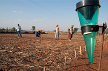 Long shot of people working on a field with a rain gauge in the foreground